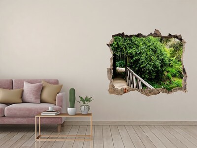 Wandsticker 3D gat met uitzicht Een groen paradijs met een houten brug.